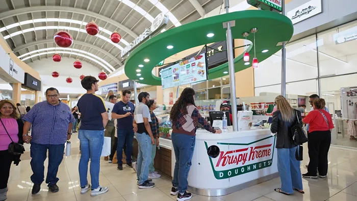 Fila de clientes en Krispy Kreme disfrutando de un postre durante su día de shopping